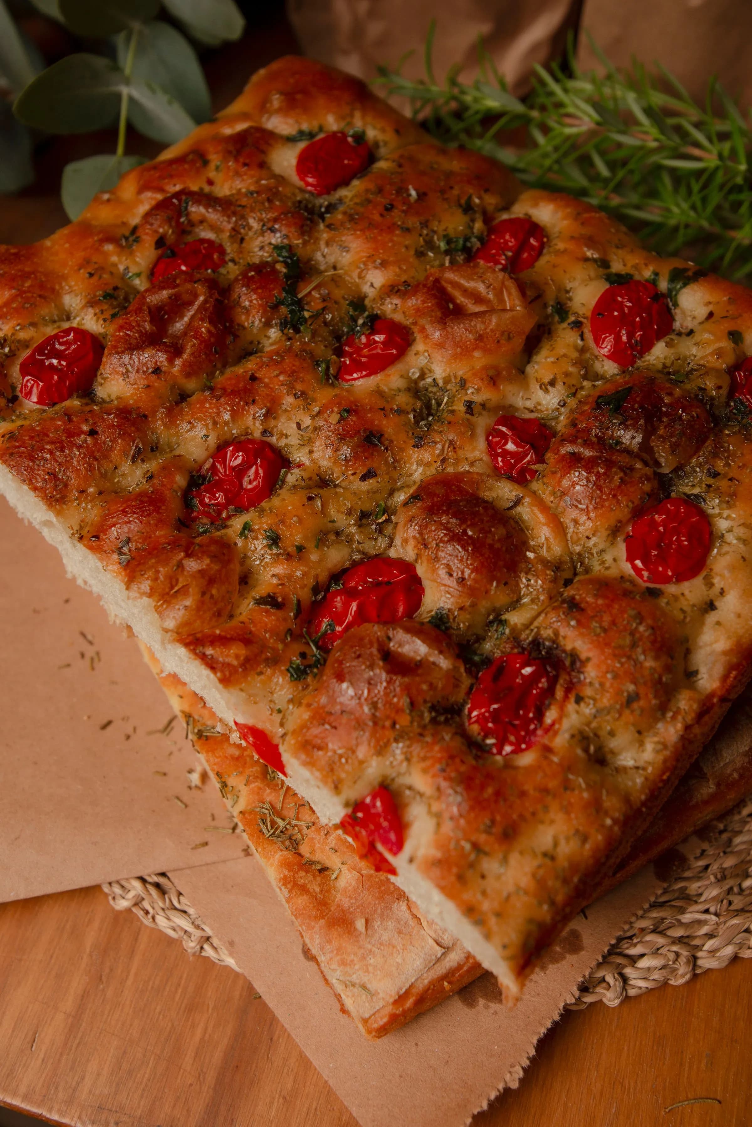 Coca dorada recién horneada con tomates cherry y hierbas frescas sobre papel kraft y romero
