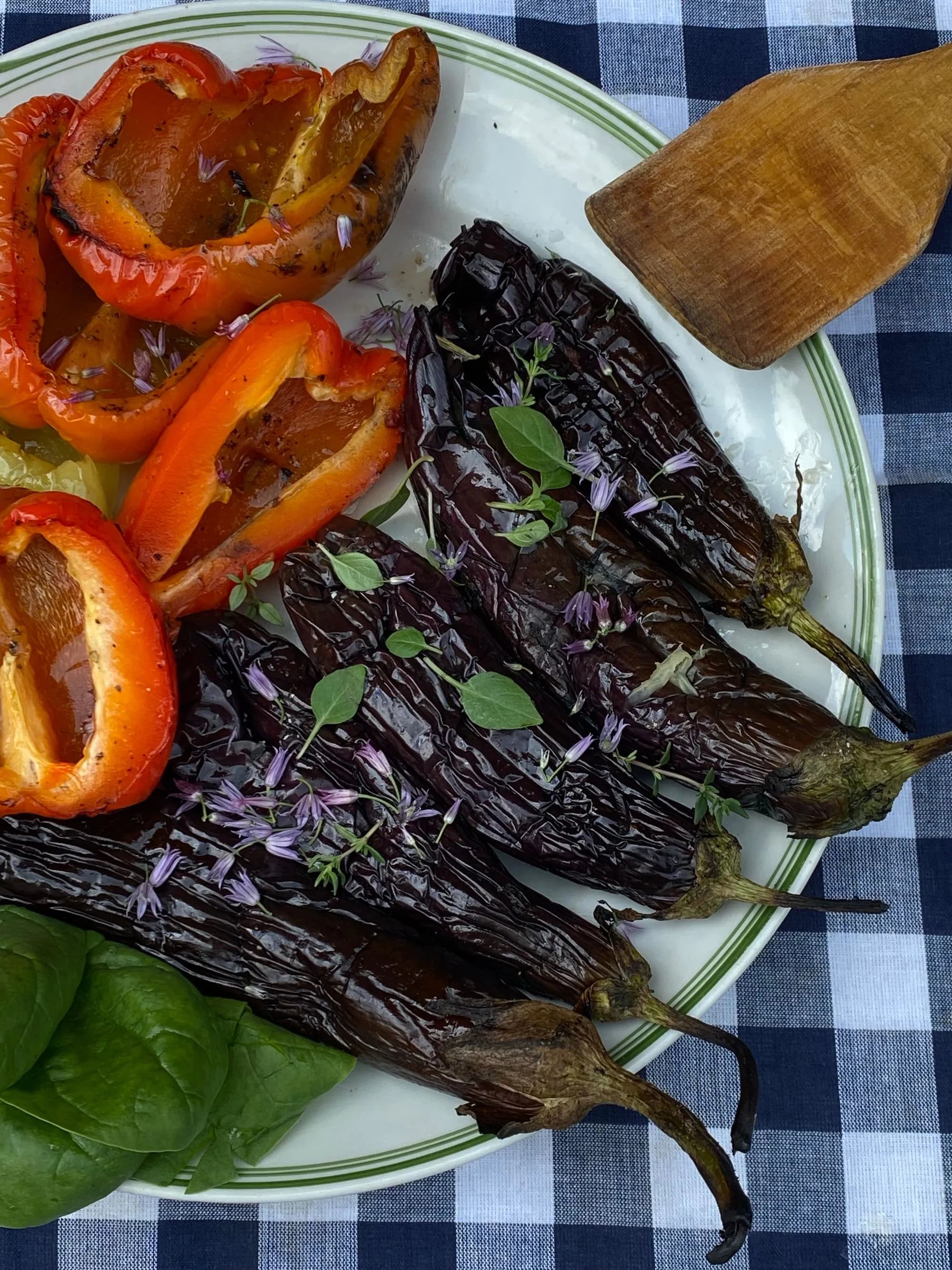 Escalivada de pimientos rojos y berenjenas asados al kamado, pelados y brillantes de aceite de oliva, con hierbas frescas por encima.