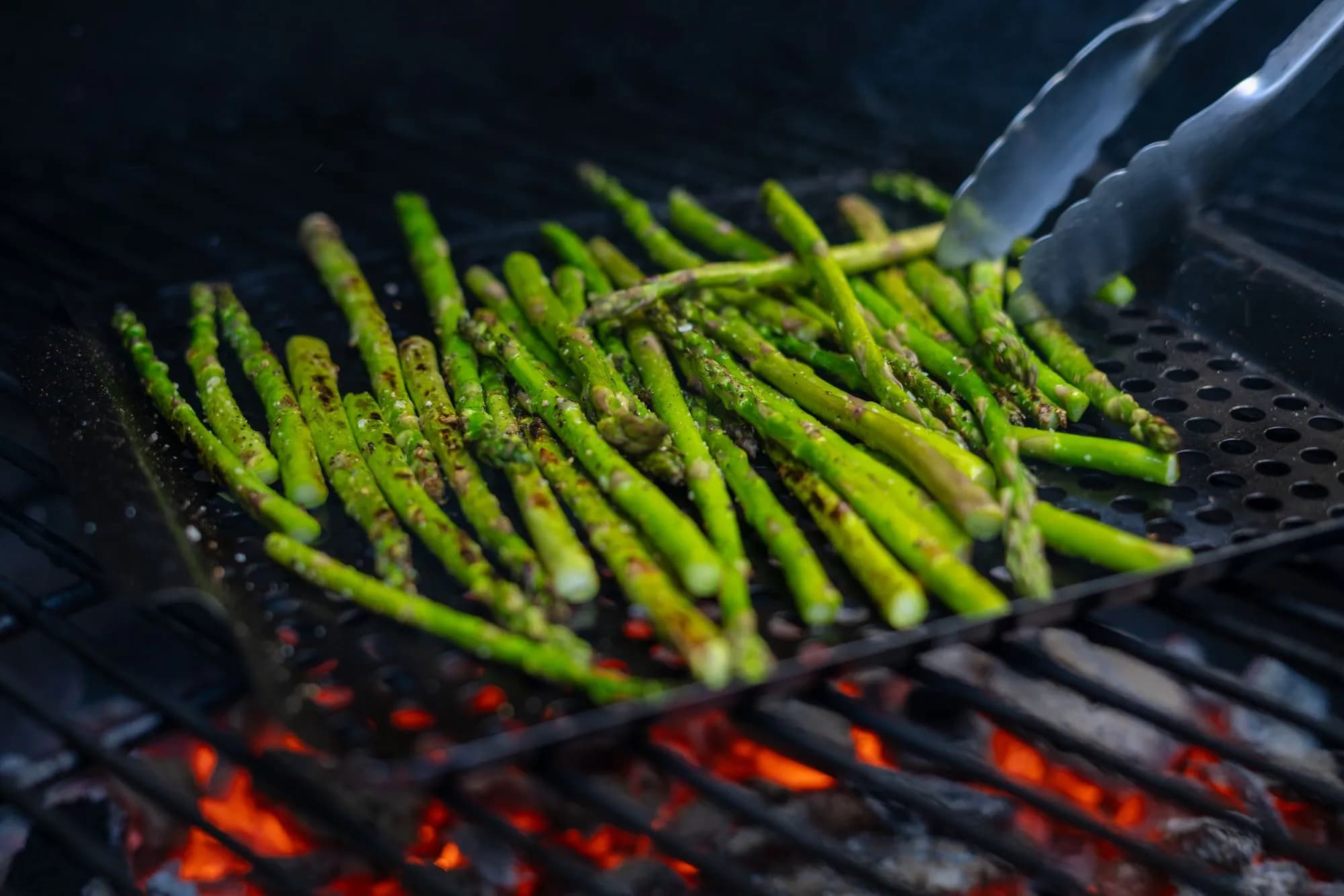 Espárragos trigueros marcados a la brasa sobre la rejilla de un kamado, con ralladura de limón y escamas de sal, algunos envueltos en jamón serrano.