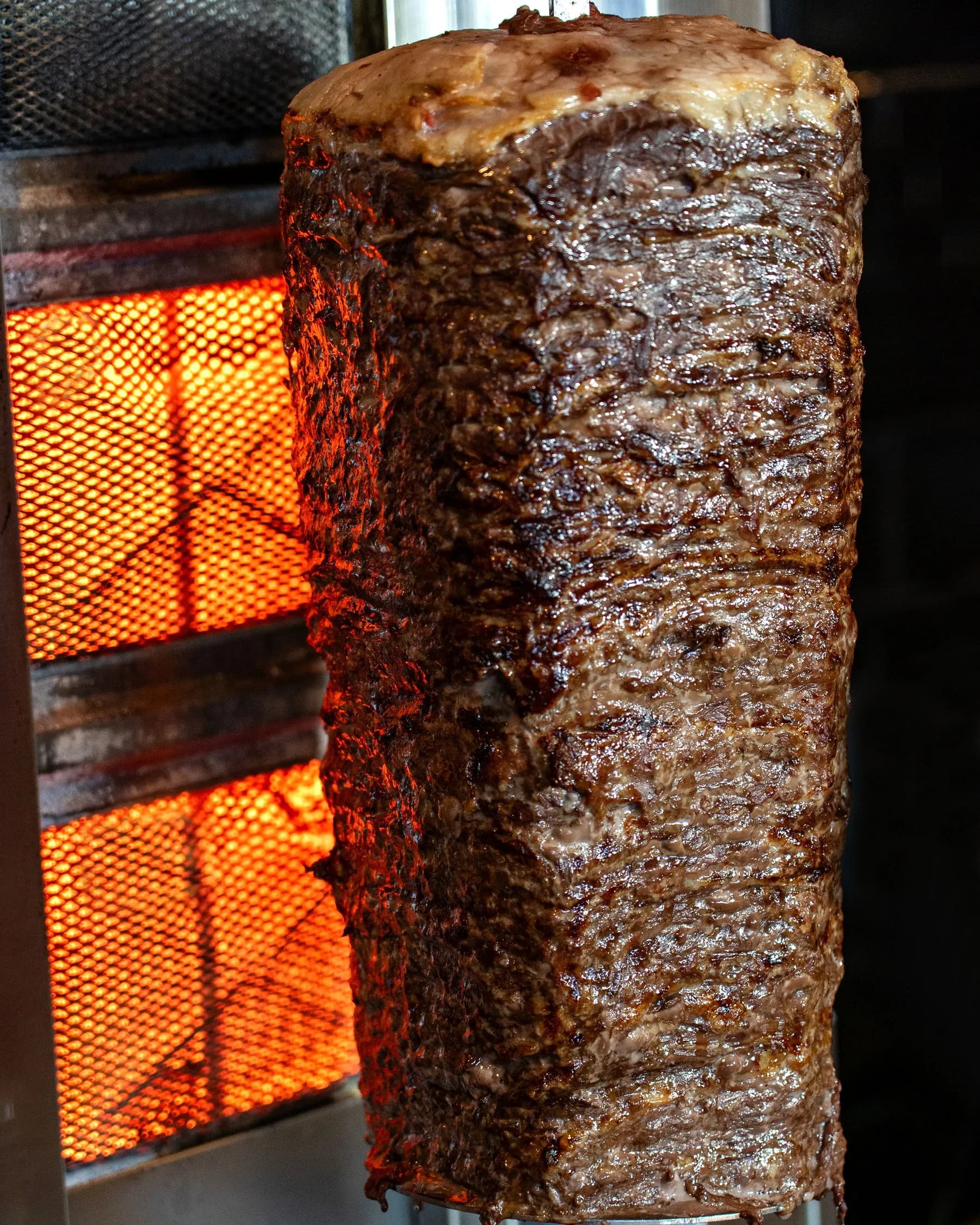 Bloque de gyros girando en el asador vertical, con la cara exterior tostada lista para cortar