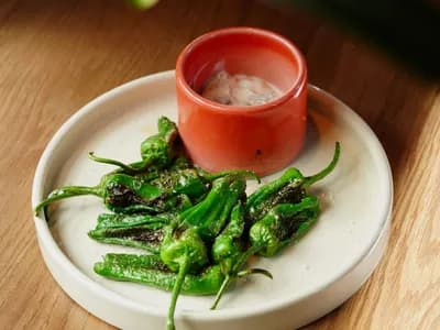 Pimientos de Padrón brillantes de aceite y con la piel ampollada, recién salteados en una sartén de hierro sobre un kamado, espolvoreados con sal en escamas.