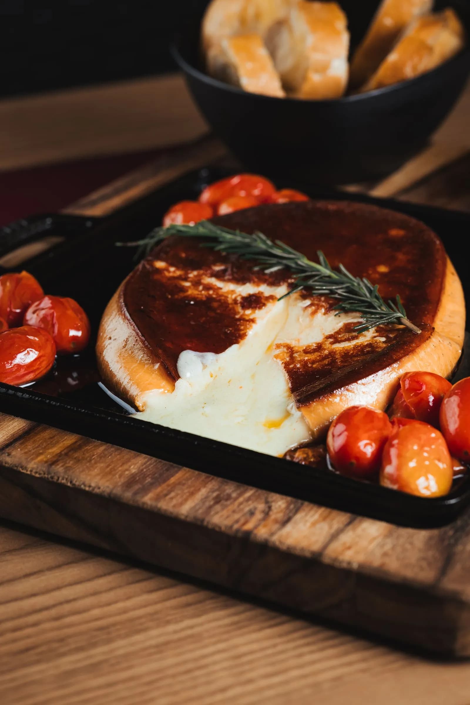 Rueda de provolone fundido a la brasa en sartén de hierro fundido con tomates cherry asados y una ramita de romero