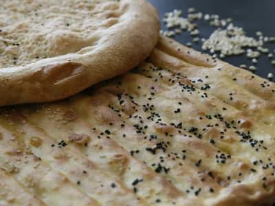 Naan recién horneado y ampollado, pincelado con mantequilla de ajo y espolvoreado con cilantro, sobre una piedra junto a un kamado de cerámica.