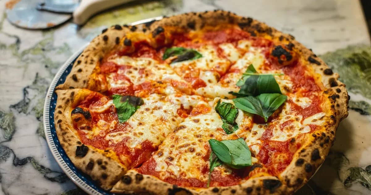 Pizza margherita con albahaca fresca y cornicione moteado, recién salida del kamado