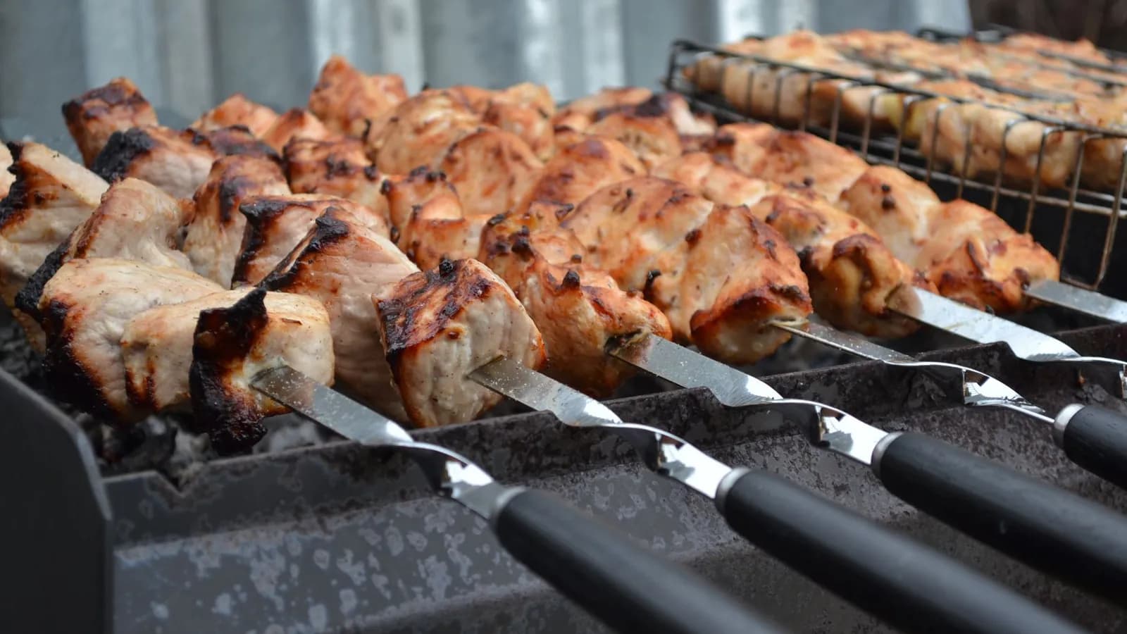 Brochetas de cuello de cerdo doradas sobre pinchos metálicos, asándose sobre las brasas